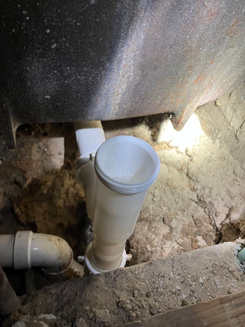 Image of plumbing pipes and fittings in a basement, featuring a white PVC pipe connection.