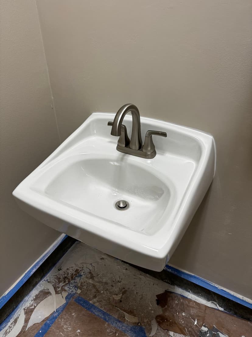 Wall-mounted white sink with modern faucet in partially renovated bathroom.